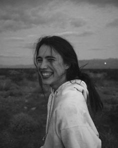 black and white photograph of a woman smiling in the middle of an open field with clouds