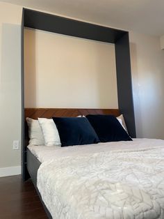 a bed with white and blue pillows on top of it in a room that has wood flooring