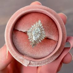 someone is holding an engagement ring in a pink velvet box that has a large diamond on it