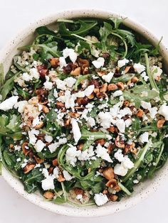 a white bowl filled with salad topped with feta cheese and walnuts on top