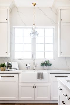 a kitchen with white cabinets and marble counter tops, along with a gold chandelier hanging from the ceiling