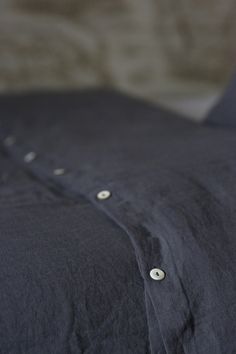 an unmade bed with black sheets and buttons on the pillow cover is seen in this close up photo