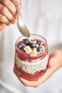 a person holding a spoon in a jar filled with fruit and oatmeal