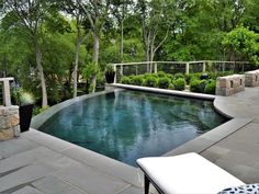 an outdoor swimming pool surrounded by trees and shrubs with patio furniture on the other side