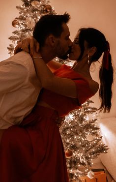 a man and woman kissing in front of a christmas tree