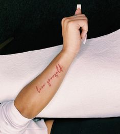 a woman with a small tattoo on her arm holding onto a white pillow that says love yourself