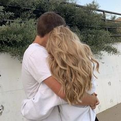 a man and woman hugging each other in front of a wall with plants growing on it