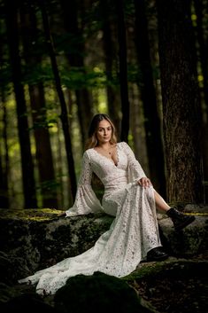 a woman sitting on top of a rock in the woods wearing a white dress and black boots