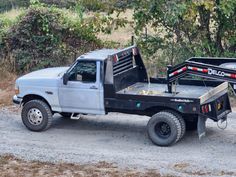 a flatbed truck parked on a dirt road next to some bushes and trees in the background