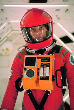 a man in an orange space suit with a radio on his chest and wearing a red helmet