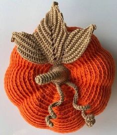 an orange knitted pumpkin with a crochet leaf decoration on it's top