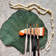 five brushes are arranged on top of a leaf with beads hanging from the end, along with two necklaces