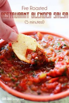 a hand dipping a tortilla chip into a bowl of salsa