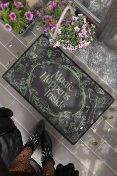 a woman is standing in front of a door mat that says magic happens inside and has flowers growing out of it