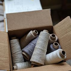 a cardboard box filled with lots of different colored spools of thread on top of each other