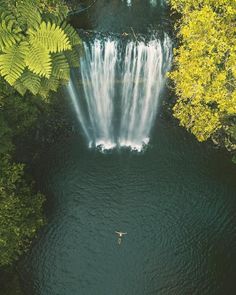 an aerial view of a waterfall in the middle of a river with trees surrounding it