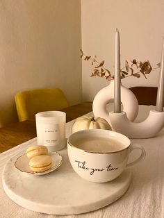 a white table topped with a bowl and plate filled with food next to a candle