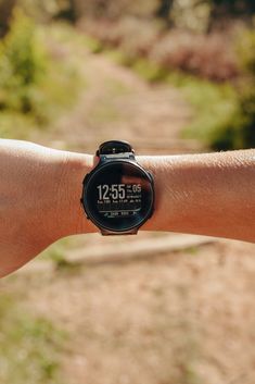 a person's arm with a smart watch on it, in the foreground is a dirt path