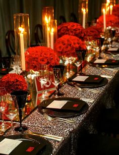 a long table is set with red roses and black place settings for dinner guests to enjoy