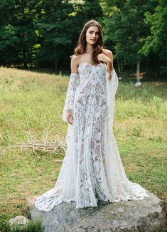 a woman standing on top of a rock wearing a white wedding dress with long sleeves