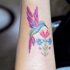 a colorful hummingbird tattoo on the wrist with flowers and leaves around it's neck