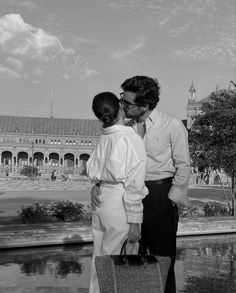 a man and woman standing next to each other in front of a building with a fountain