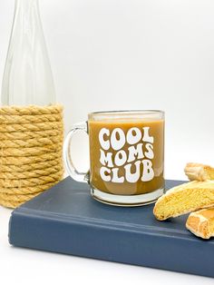 a coffee mug with the words cool moms club on it next to some cookies