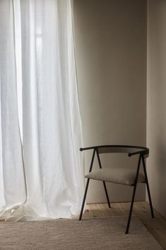 a chair sitting in front of a window next to a white curtain and wooden floor