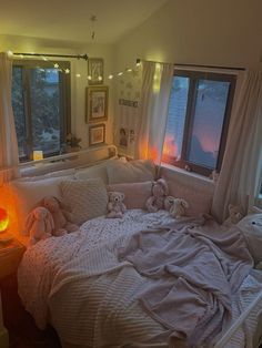 a bed with two teddy bears sitting on it in front of some windows and lights