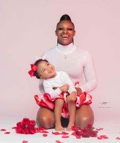 a woman holding a baby in her lap and sitting on the floor with rose petals