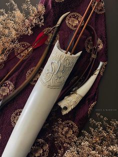 an assortment of different types of archery bows and arrows laying on a purple cloth with flowers