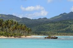 an island surrounded by palm trees in the middle of water with mountains in the background