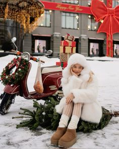 a woman sitting on top of a christmas tree next to a scooter in the snow