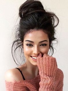 a woman with her hand on her face and wearing an off the shoulder knitted sweater