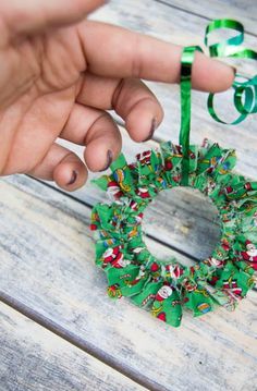 a hand holding a green ribbon around a wreath ornament on a wooden table