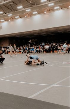 two men wrestling in an indoor gym with people watching from the sidelines and onlookers