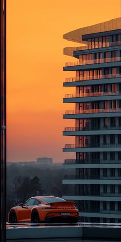 an orange sports car is parked in front of a tall building with balconies