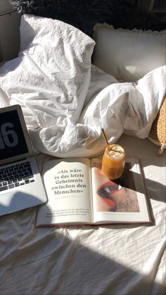 an open laptop computer sitting on top of a bed next to a book and drink