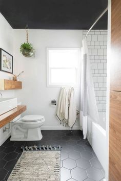 a white toilet sitting next to a bathroom sink under a window in a room with black and white tiles