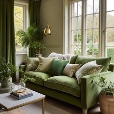 a living room filled with lots of green furniture and plants in front of large windows