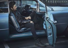 a man sitting in the driver's seat of an old car with his foot propped up