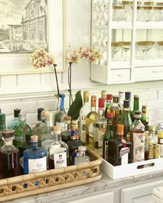 bottles and glasses are lined up on the counter in front of an art piece with flowers