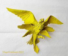 a yellow bird made out of paper sitting on top of a white wall with it's wings spread wide open