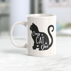 a white coffee mug with a black cat design on the front and bottom, says crazy cat dad