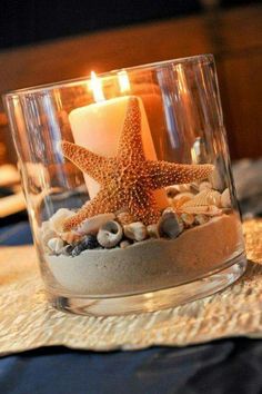 a candle that is sitting in a glass bowl with sand and shells on the table