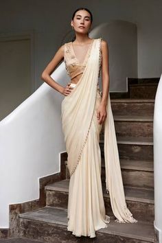 Beige pre-draped plain saree with nalki, pearl beads embellished border. Paired with sleeveless V neck padded blouse with nalki, pearls, stones, crystals, sequin floral clusters embroidery.
Components: 2
Pattern: Embroidery
Type Of Work: Nalki, Pearls, Stones, Crystals, Sequin
Neckline: V Neck
Sleeve Type: Sleeveless
Fabric: Viscose Georgette Satin, Lining: Shantoon
Color: Beige
Other Details: 
Attached inner lining
Padded blouse
Weight: 0.5kgs
Length: 42inches
Model Height: 5ft 8inches, wearing South Indian White Sari Look, Beige Saree Party Wear, Party Sarees Elegant, Beige Saree Look, Sari Inspired Wedding Dress, V Neck Blouse Indian Sleeveless, High Standards Woman Aesthetic, Halter Blouse Saree, Plain Saree Look