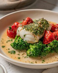 a white plate topped with fish and broccoli covered in sauce on top of a table