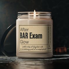 a candle that is sitting on a table next to a black container with the words after bar exam glow written on it