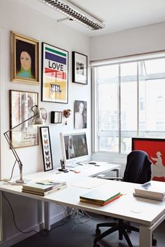 a white desk topped with a laptop computer next to a window covered in framed pictures