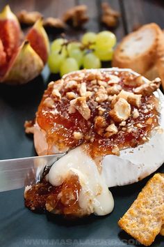 a piece of cheese covered in fruit and nuts on a black plate with a knife